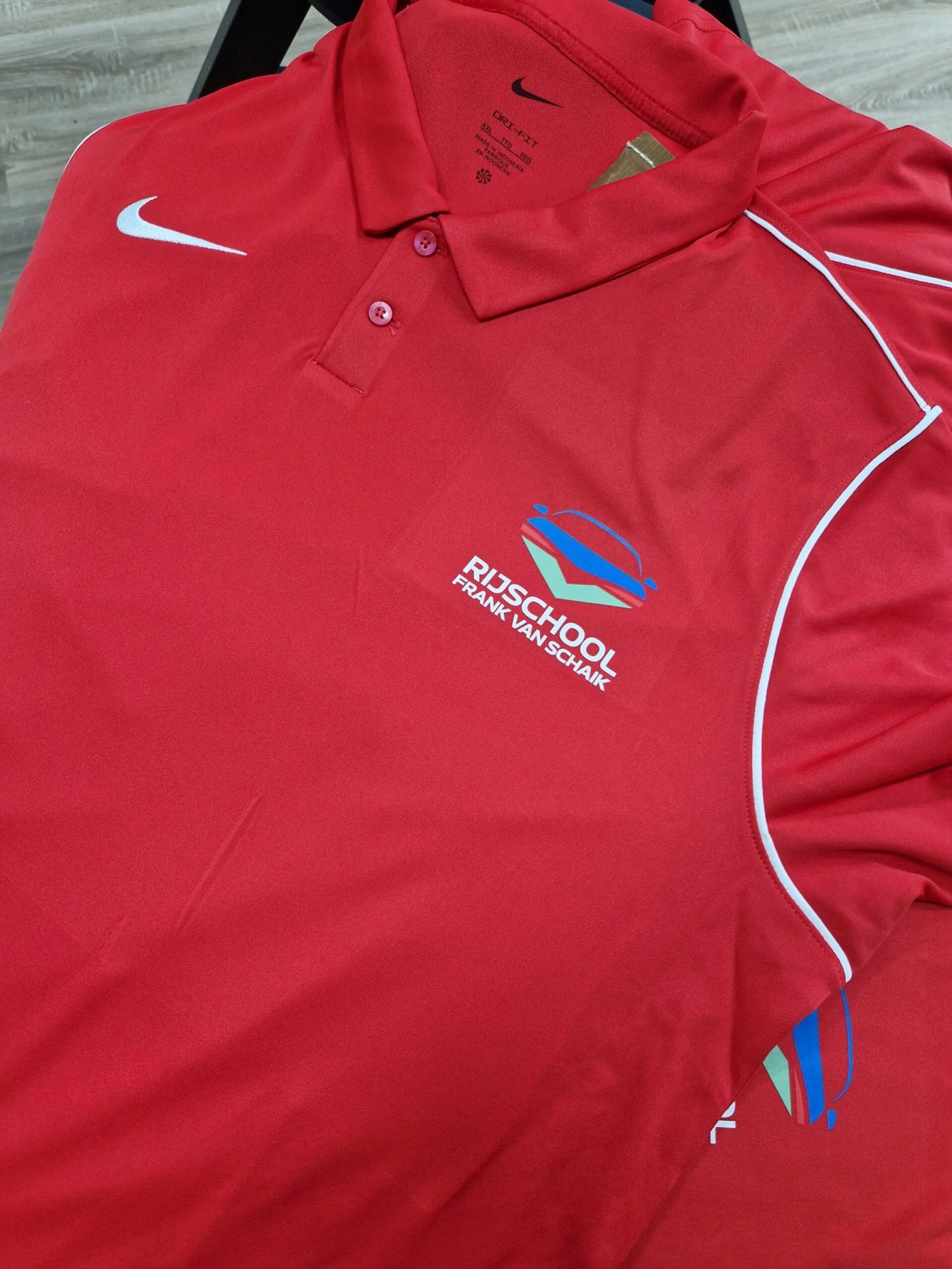 Rode sportpolo met bedrukt logo van een rijschool